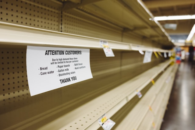 Empty shelves in supermarket with sign listing high demand items
